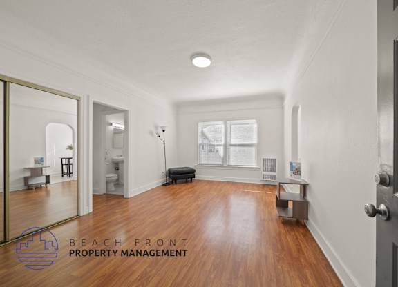 A spacious room with wooden floors and a large mirror on the wall.