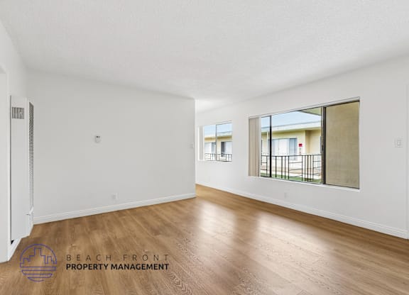A spacious room with wooden flooring and a view of a balcony through a window.