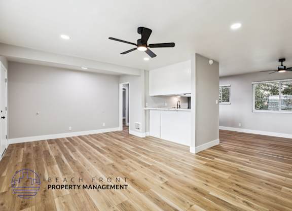 A spacious room with wooden floors and two ceiling fans.