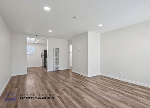 A spacious room with wooden flooring and white walls, with a logo for Beach Front Property Management in the bottom left corner.