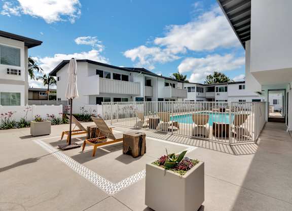 A sunny day at a poolside with chairs and a table.