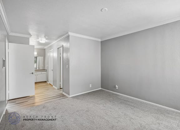 A spacious room with a carpeted floor and white walls, with a doorway leading to another room.