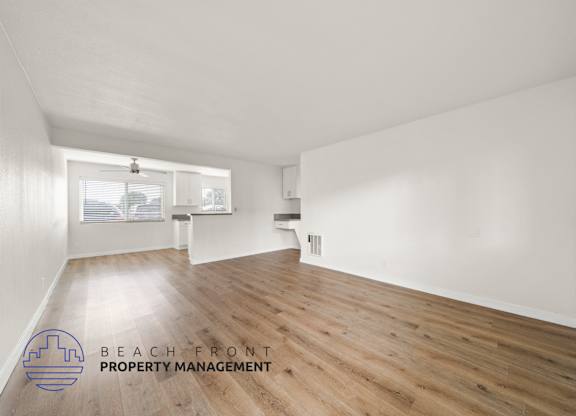 A spacious room with wooden flooring and white walls, with a window and a door visible.