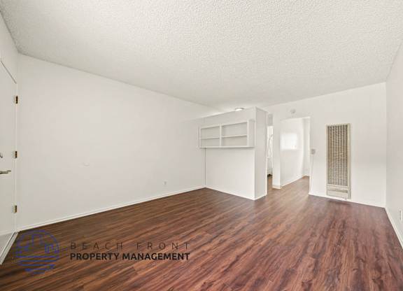 A room with wooden floors and white walls, with a logo for Beach Front Property Management in the bottom left corner.