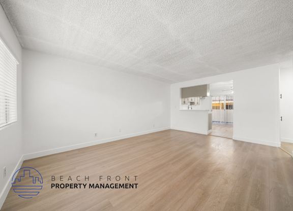 A spacious room with wooden flooring and white walls, with a logo for Beach Front Property Management in the bottom left corner.