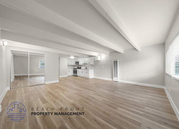 A spacious room with wooden flooring and white walls, with a logo for Beach Front Property Management in the bottom left corner.