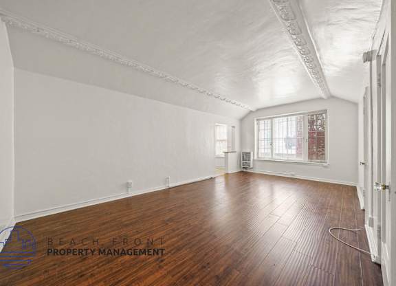 A room with wooden floors and white walls, with a window and a door visible.