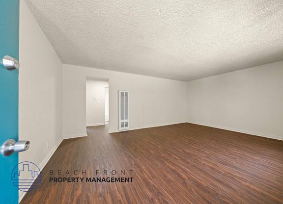 A room with wooden floors and white walls, with a door in the background.