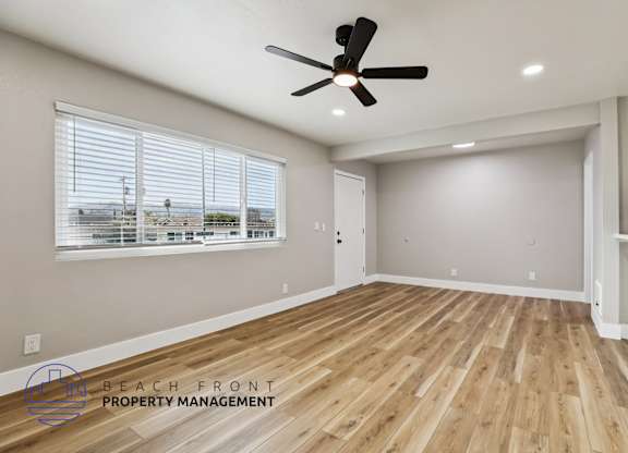A spacious room with wooden flooring and a ceiling fan.