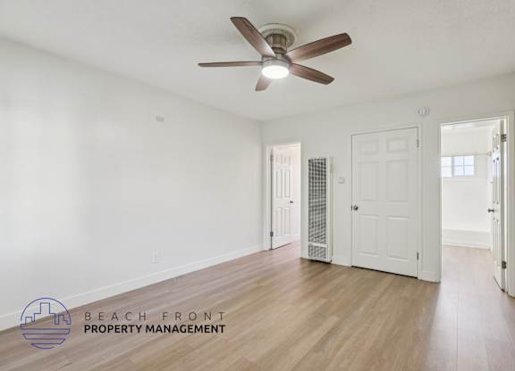A room with a ceiling fan and wooden floors, with a logo for Beach Front Property Management in the bottom left corner.
