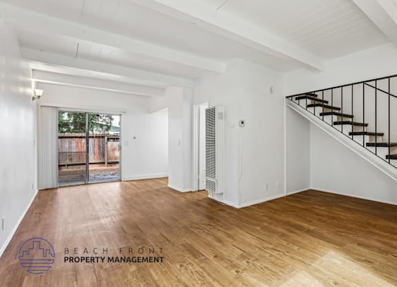 A spacious room with wooden floors and a staircase with a metal railing.