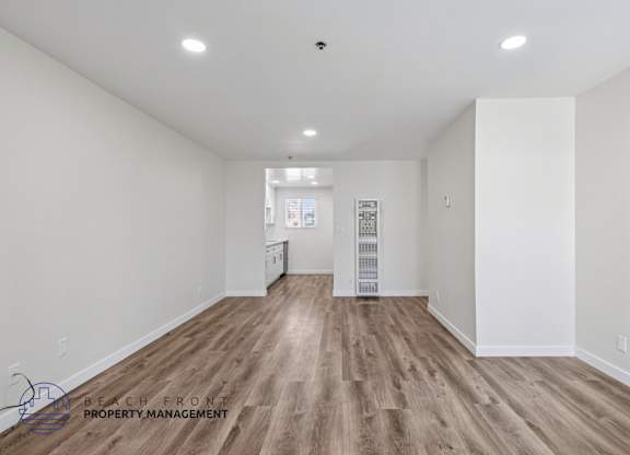 A spacious room with wooden flooring and white walls.