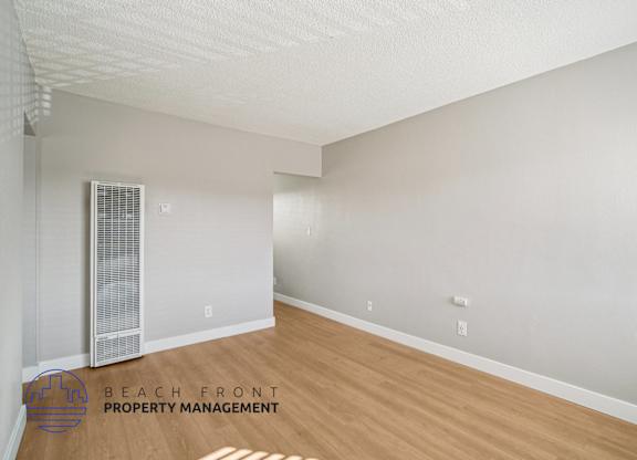 A spacious room with a wooden floor and a window with blinds.