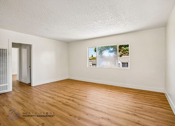 A room with wooden flooring and a window showing a view of trees and a building.