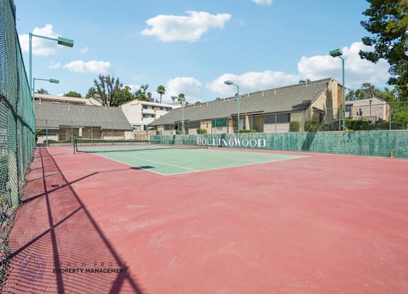 A red tennis court with a green fence and the words