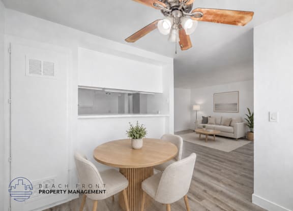 A dining room with a round table and chairs, a ceiling fan, and a living room with a couch in the background.
