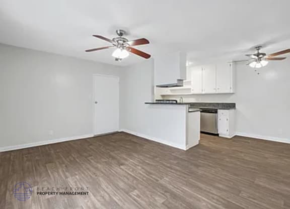 A spacious room with a kitchenette and two ceiling fans.