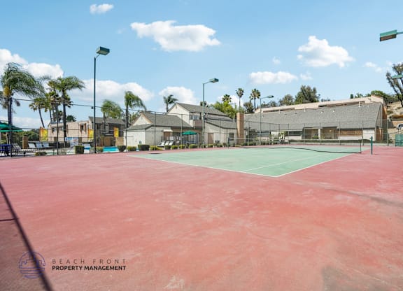 A tennis court with a red surface and a green court in the background.