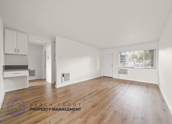 A spacious room with wooden flooring and white walls, with a logo for Beach Front Property Management in the bottom left corner.