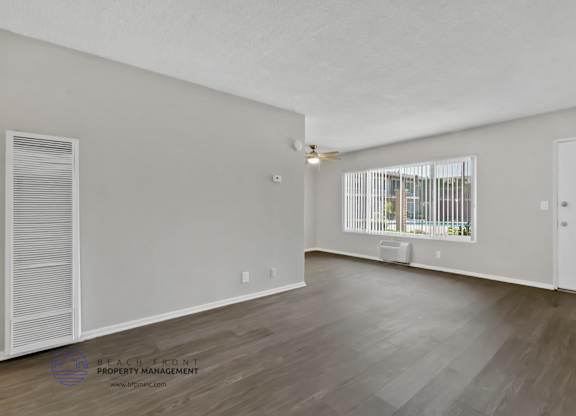 A spacious room with wooden flooring and a window with blinds.