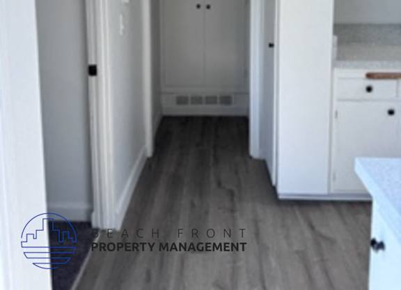 A hallway with a door at the end and a logo for Beach Front Property Management in the bottom left corner.