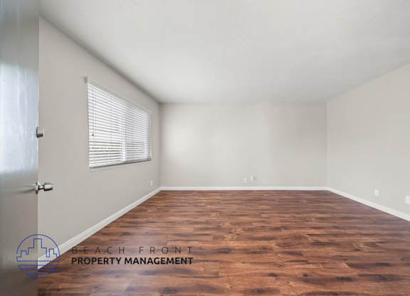 A room with wooden flooring and a window with blinds.