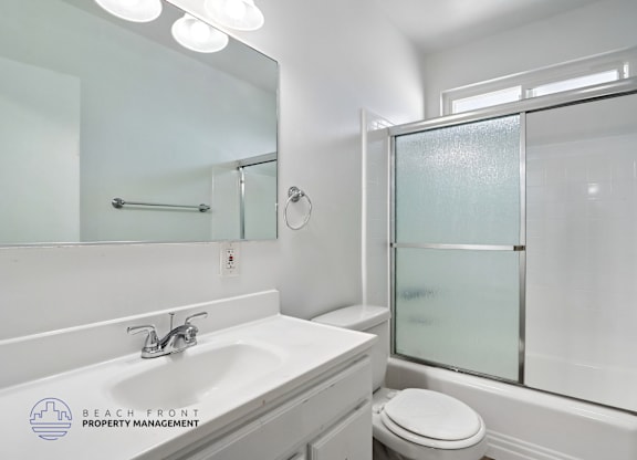 A white bathroom with a sink, toilet, and shower.