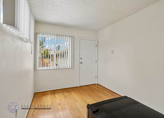 A room with a window covered by blinds, a door, and a wooden floor.