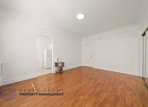 A room with wooden floors and white walls, with a logo for Beach Front Property Management in the bottom left corner.