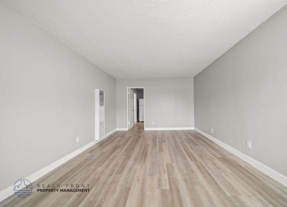 A spacious room with wooden flooring and white walls, with a doorway leading to another room.