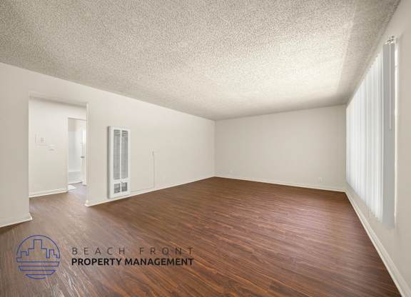 A room with wooden floors and white walls, with a logo for Beach Front Property Management in the bottom left corner.