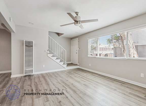 A spacious room with a ceiling fan and a staircase leading to another floor.