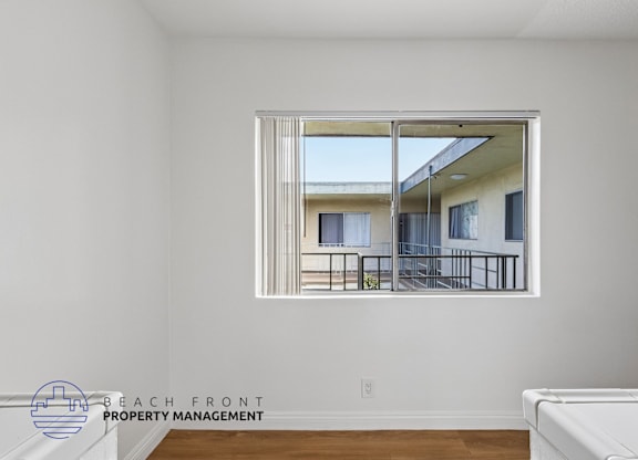A room with a large window showing a balcony with chairs and a table.