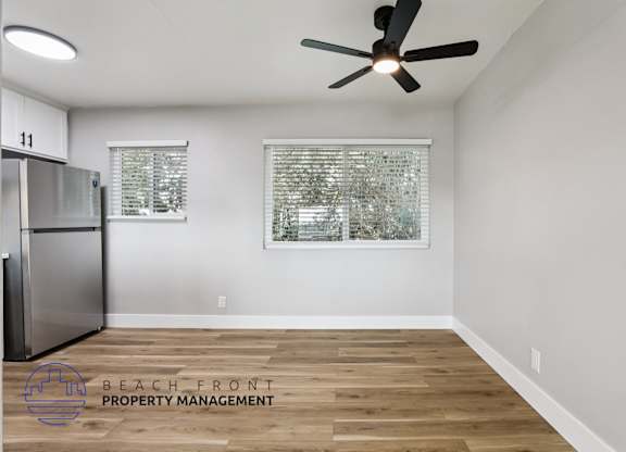 A room with a ceiling fan and a fridge in it.