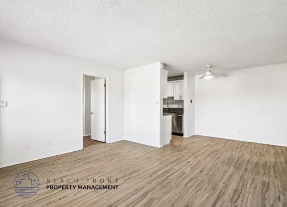 A room with wooden flooring and white walls, with a logo for Beach Front Property Management in the bottom left corner.