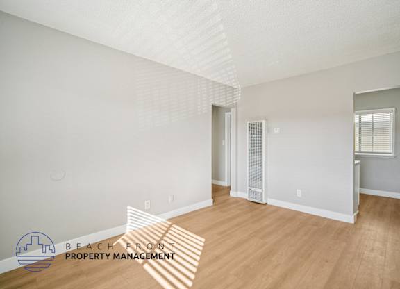 A room with wooden floors and white walls, with a window on the right wall.