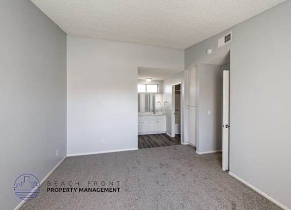 A spacious room with a carpeted floor and white walls, with a doorway leading to another room.