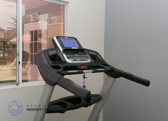 A treadmill with a digital display and control panel is in front of a window.