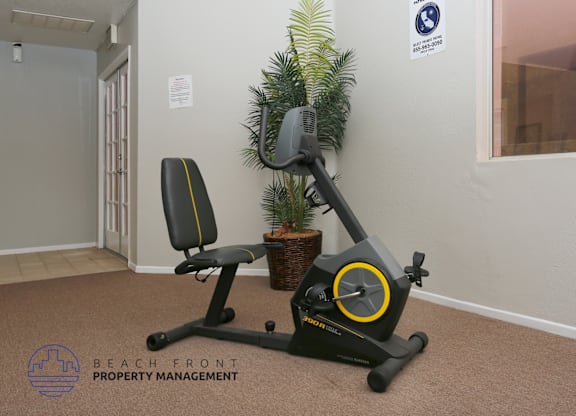 A stationary exercise bike is placed in a room with a potted plant and a sign on the wall.