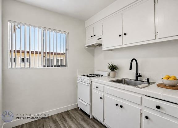A kitchen with white cabinets and a window with blinds.