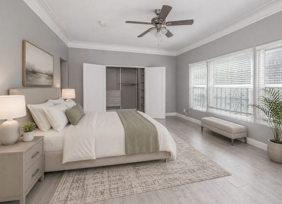 A bedroom with a large bed, a ceiling fan, and a window with blinds.