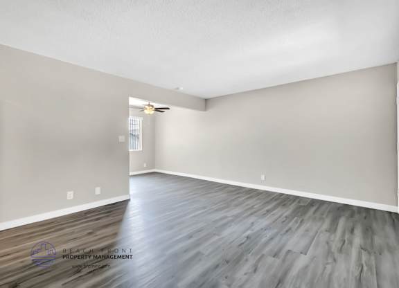 A spacious room with wooden flooring and white walls.