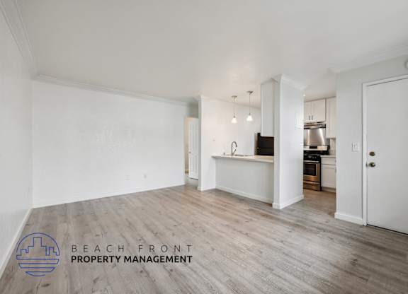 A spacious room with wooden flooring and a kitchen area in the background.