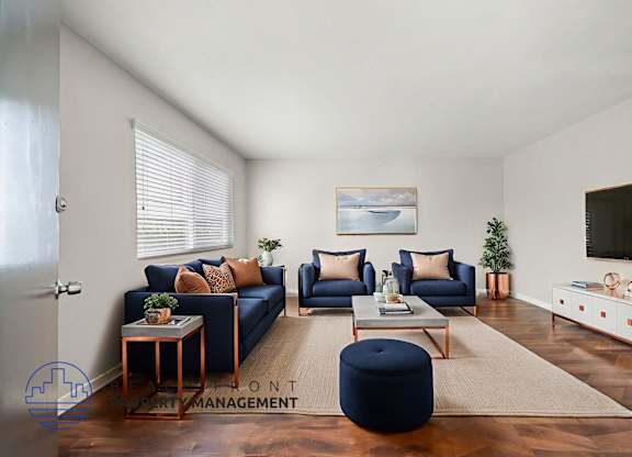 A living room with a blue ottoman and a television on the wall.