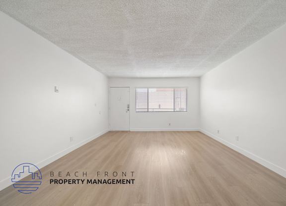 A spacious room with wooden flooring and a window with blinds.