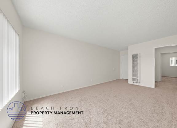 A spacious room with carpeted floor and white walls, with a logo for Beach Front Property Management in the bottom left corner.
