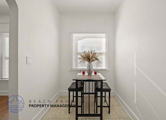 A dining table with two chairs is in a white room with a window.