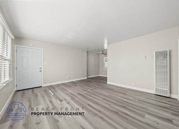 A spacious room with wooden flooring and a logo for Beach Front Property Management.