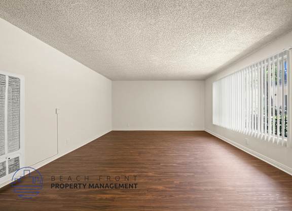 A room with wooden floors and white walls, with a window on the right side.
