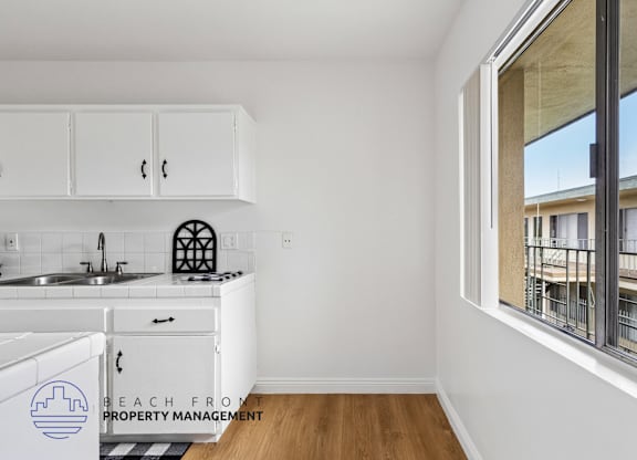 A kitchen with white cabinets and a window overlooking a balcony.
